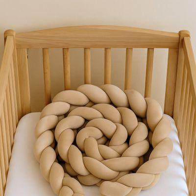 Contour de lit bébé beige placé dans un berceau en bois.