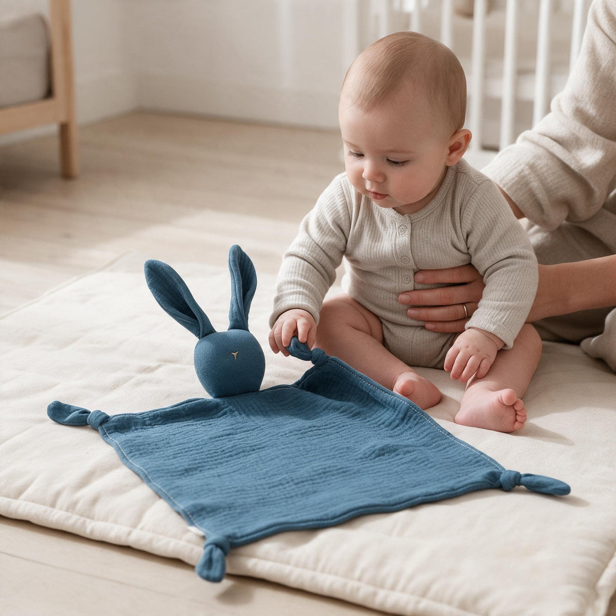 Bébé assis sur un tapis d'éveil attrapant son doudou lapin bleu par un coin noué