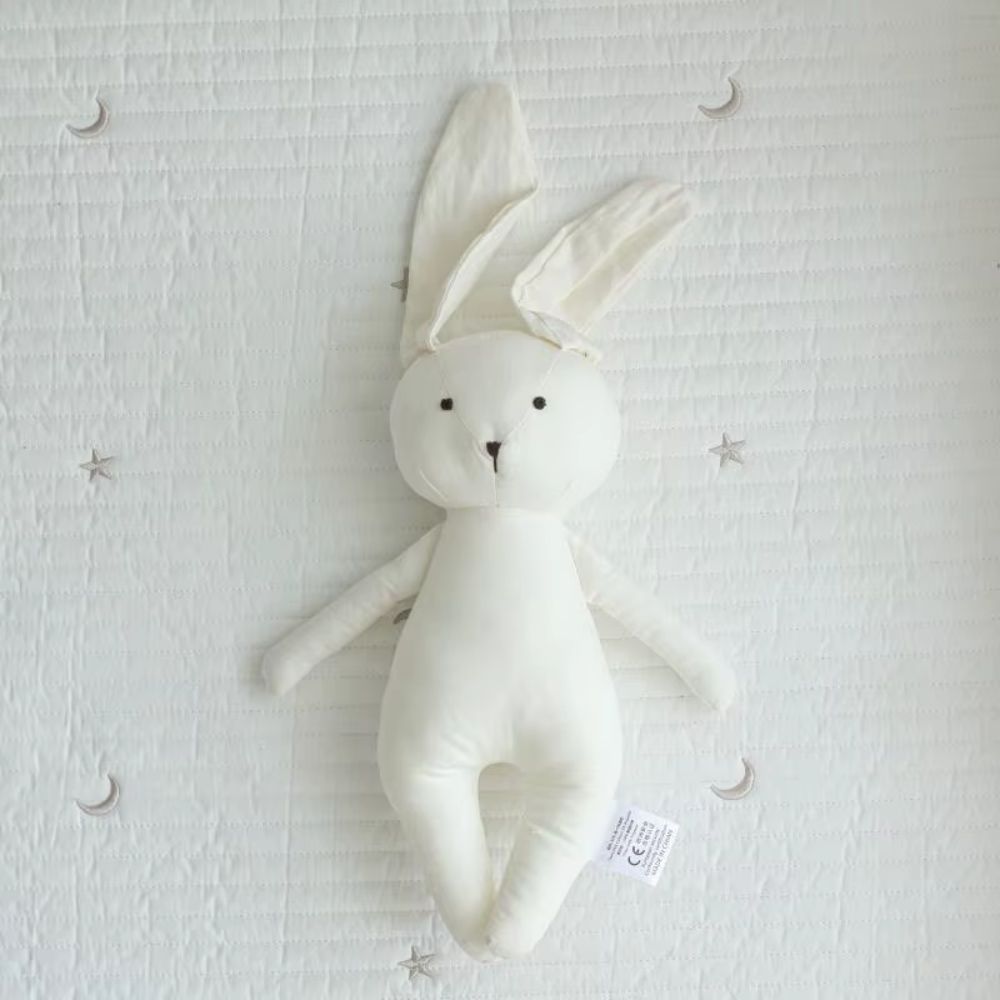 peluche bébé lapin de couleur blanche déposé sur un lit de bébé