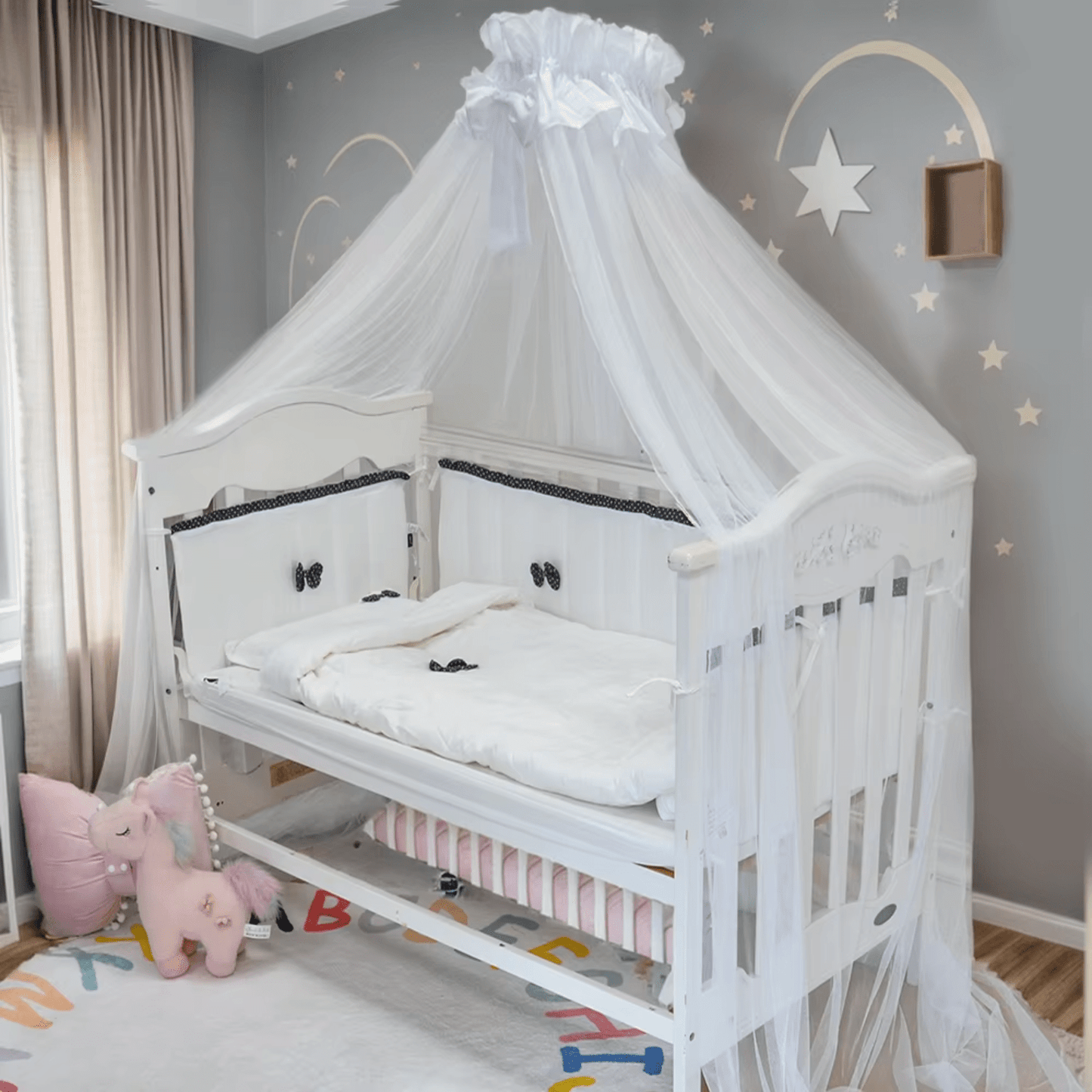Tour de lit bébé blanc avec nœuds noirs installé dans un berceau en bois clair.