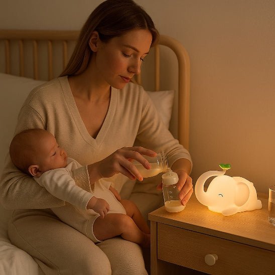 Maman assise au bord du lit tenant son bébé, tend le bras vers la table de chevet pour verser le lait dans le biberon à la lueur de la veilleuse éléphant