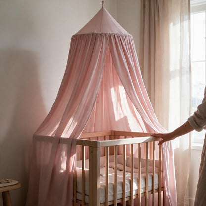 Ciel de lit bébé Rêverie rose poudré suspendu au-dessus d'un berceau en bois