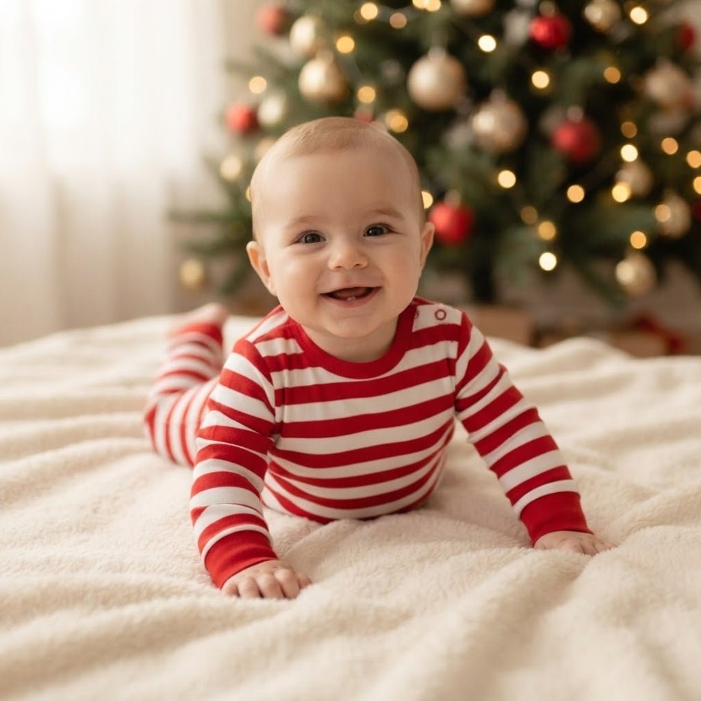 Bébé souriant en grenouillère rayée rouge et blanc Sucre d'Orge devant le sapin de Noël