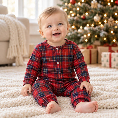 Bébé en grenouillère de Noël tartan rouge à pressions devant le sapin