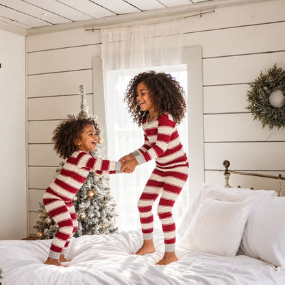 Enfants en pyjama de Noël rayé rouge et blanc qui sautent sur le lit
