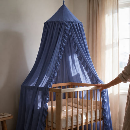 Ciel de lit à volants bleu Myrtille au-dessus d'un lit bébé près d'une fenêtre