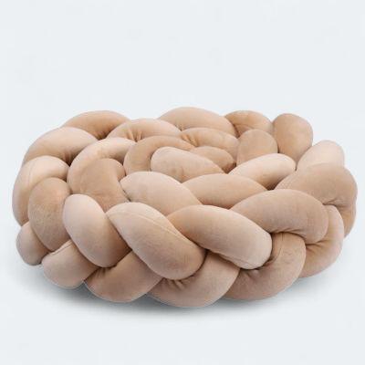 Coussin tressé en velours beige servant de contour de lit bébé.