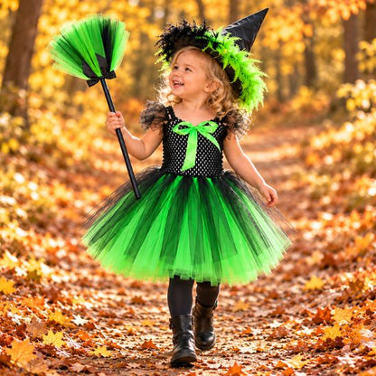 Tout‑petite en costume sorcière vert qui marche en riant avec son balai dans les feuilles d'automne