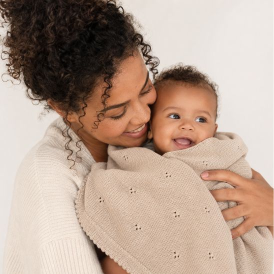 Bébé blotti contre sa maman sous une couverture tricot beige