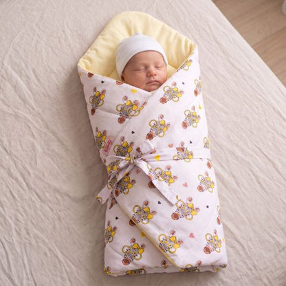 Bébé emmailloté dans une couverture motif zèbre et ballons, coiffé d'un bonnet blanc, sur un drap clair