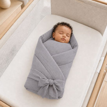 Bébé emmailloté dans une couverture d'emmaillotage grise, allongé dans un lit à barreaux