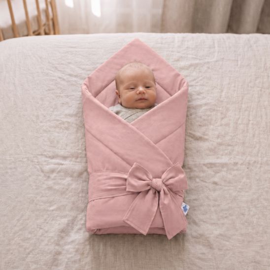 Bébé emmailloté dans une couverture unie rose poudré, allongé sur un lit