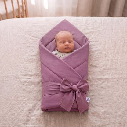 Bébé emmailloté dans une couverture unie mauve tendre, allongé sur un lit