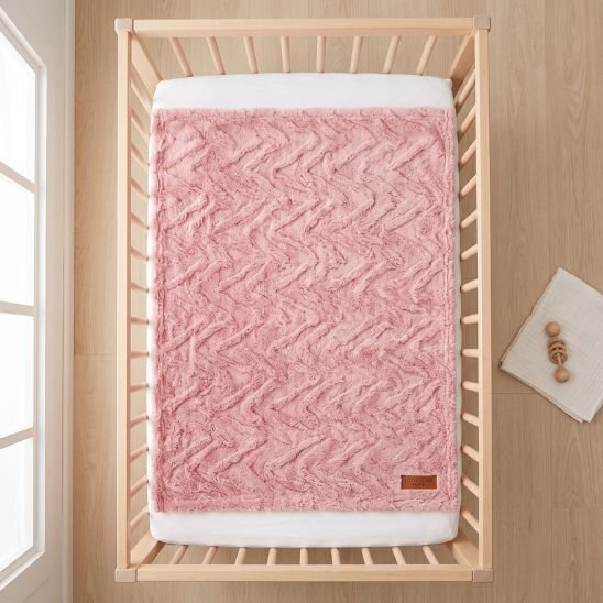 Couverture lit bébé rose dépliée dans un lit à barreaux, vue du dessus, format 80x100 cm