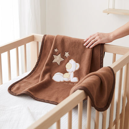 Couverture en polaire bébé marron avec ourson brodé posée sur un lit à barreaux