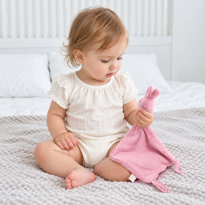 Petite fille assise tenant son doudou plat lapin rose