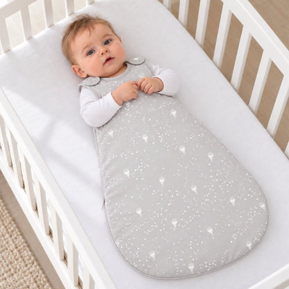 Bébé allongé dans son lit à barreaux, en gigoteuse grise étoilée
