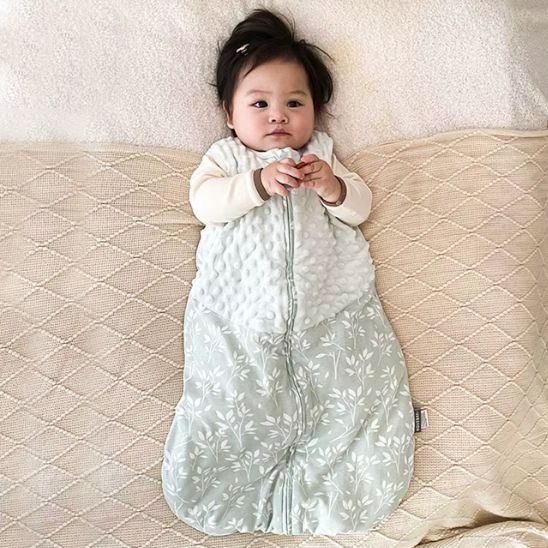 Gigoteuse sans manches bi-matière mi-saison, bébé allongé, zip central, haut matelassé blanc et bas vert sauge à motifs.