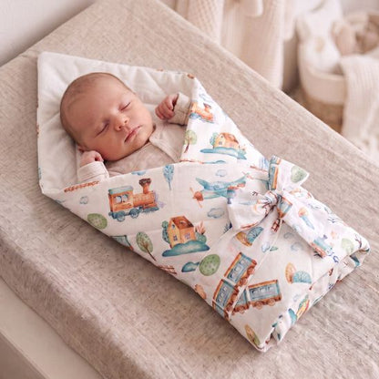Bébé emmailloté dans une gigoteuse réversible motif petit train, posé sur une table à langer