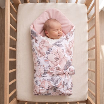 Bébé emmailloté dans une gigoteuse réversible motif fleurs roses, dans un lit à barreaux