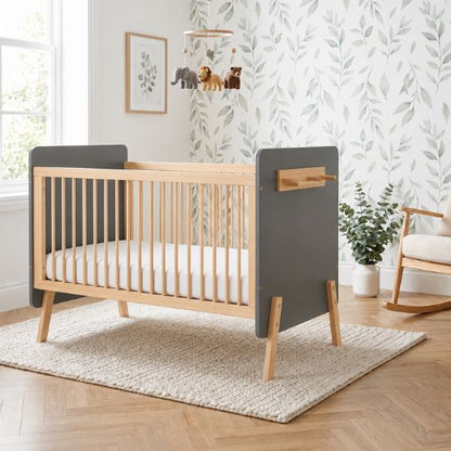 Lit bébé évolutif bois naturel et gris dans une chambre avec papier peint feuilles et mobile animaux