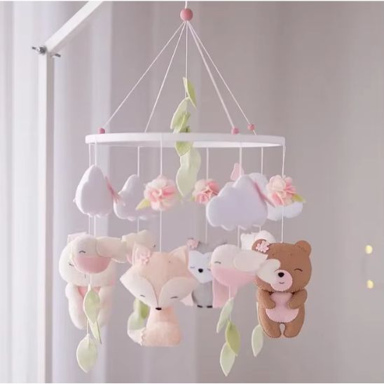 Mobile bébé fille en bois blanc avec figurines en feutrine rose pastel, suspendu au-dessus d’un berceau.