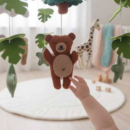 Mobile bébé animaux doux — main de bébé qui touche l'ourson en feutre sur tapis d'éveil