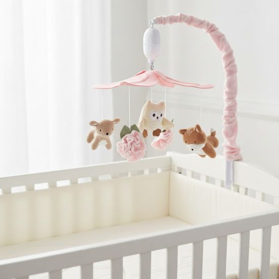 Vue latérale du mobile musical pour bébé forêt féerique fixé sur lit blanc