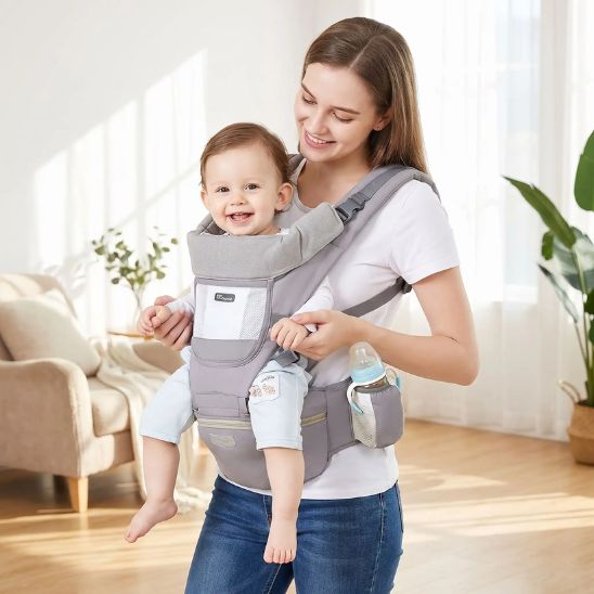 Porte bébé ergonomique gris avec siège de hanche et porte-biberon – bébé souriant porté face au monde, intérieur