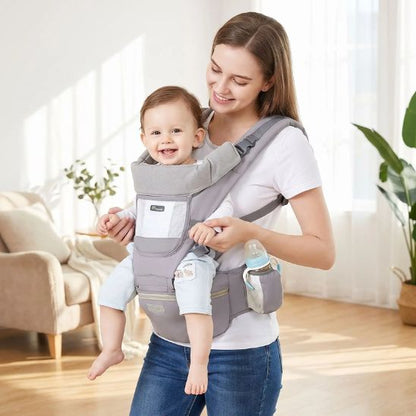 Porte bébé ergonomique gris avec siège de hanche et porte-biberon – bébé souriant porté face au monde, intérieur