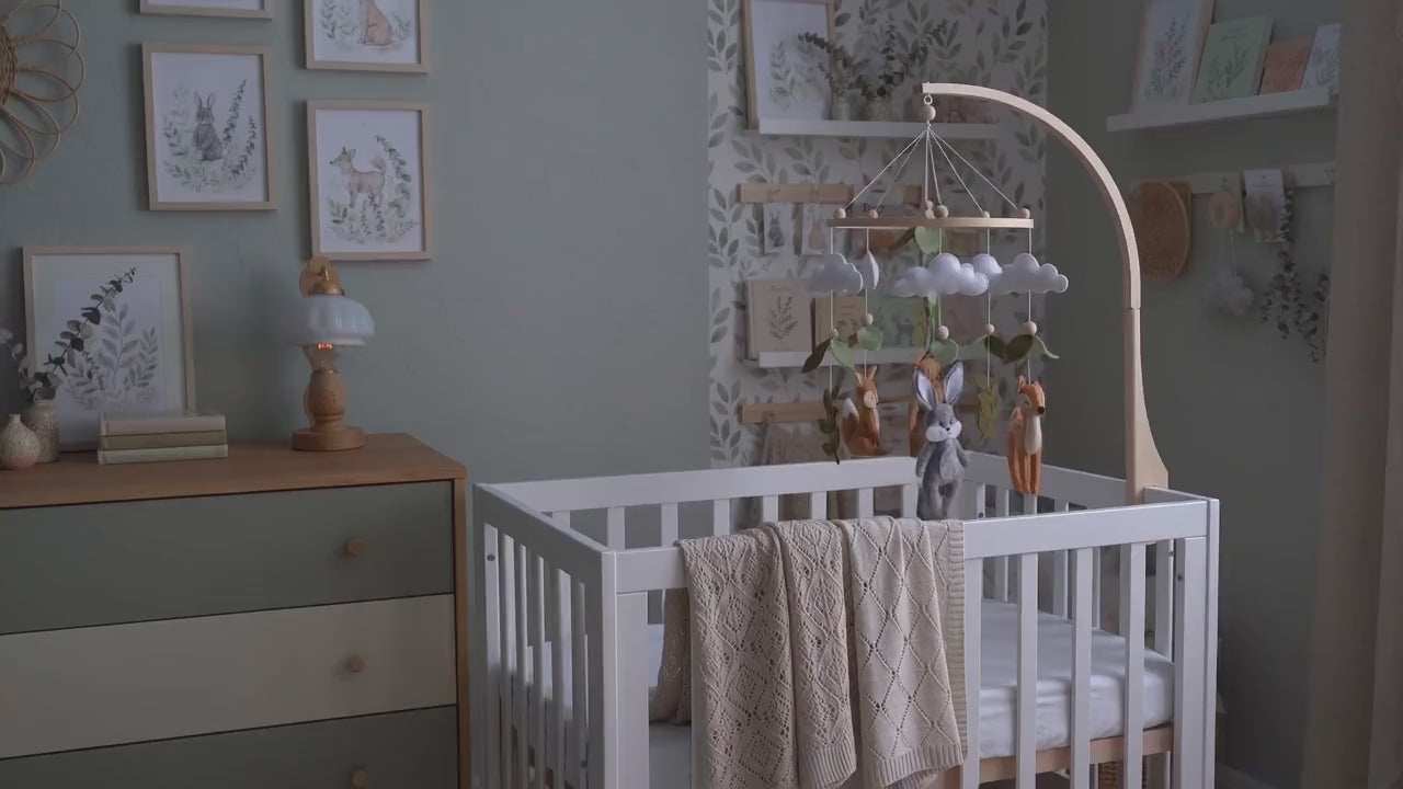 Mobile bébé forêt en feutrine qui tourne au-dessus d'un berceau dans une chambre de bébé, à la lumière douce d'une lampe