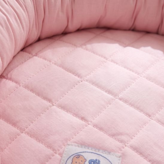 Gros plan sur la texture matelassée en coton du réducteur de lit bébé rose