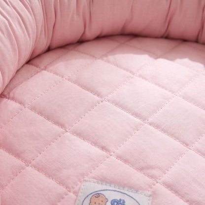 Gros plan sur la texture matelassée en coton du réducteur de lit bébé rose