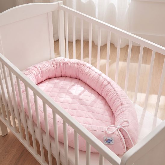 Réducteur de lit bébé rose installé dans un lit à barreaux blanc