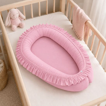 Réducteur de lit bébé à volants rose installé dans un lit à barreaux en bois