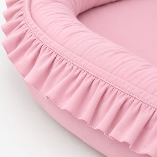 Gros plan sur les volants et la texture en coton du réducteur de lit bébé rose