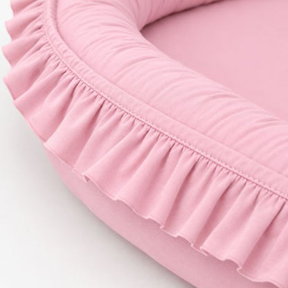 Gros plan sur les volants et la texture en coton du réducteur de lit bébé rose