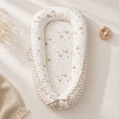 Réducteur de lit bébé motif étoiles beige posé près d'un hochet en bois et d'une couverture tricotée