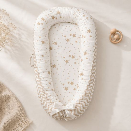Réducteur de lit bébé motif étoiles beige posé près d'un hochet en bois et d'une couverture tricotée