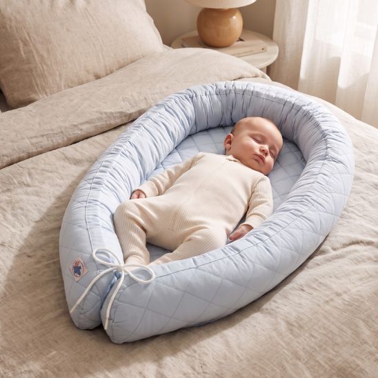 Bébé endormi dans le réducteur de lit bébé bleu ciel posé sur un lit adulte