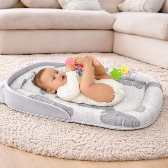 Bébé qui joue avec jouets colorés posé sur réducteur de lit bébé pliable Tropical comme matelas de sol salon