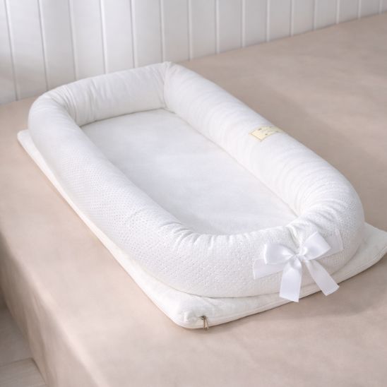Réducteur de lit bébé portable blanc sur lit adulte lumière naturelle vue latérale nœud satin
