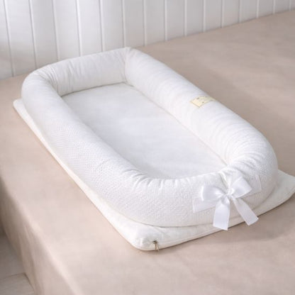 Réducteur de lit bébé portable blanc sur lit adulte lumière naturelle vue latérale nœud satin