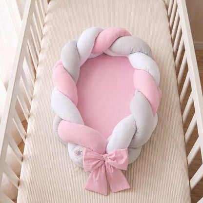 Réducteur de lit tressé rose avec matelas rose, vu de dessus dans un lit à barreaux