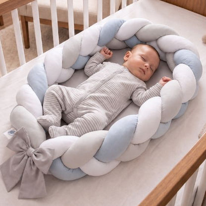 Bébé endormi vu de dessus dans un réducteur de lit tressé bleu, blanc et gris