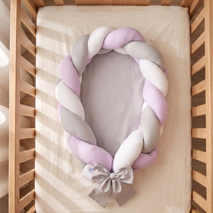 Réducteur de lit tressé lilas, gris et blanc vu de dessus dans un lit à barreaux