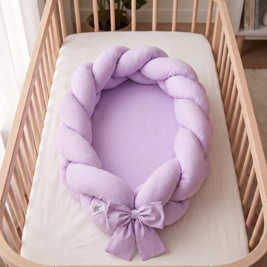 Réducteur de lit tressé lilas vu de dessus dans un lit à barreaux en bois