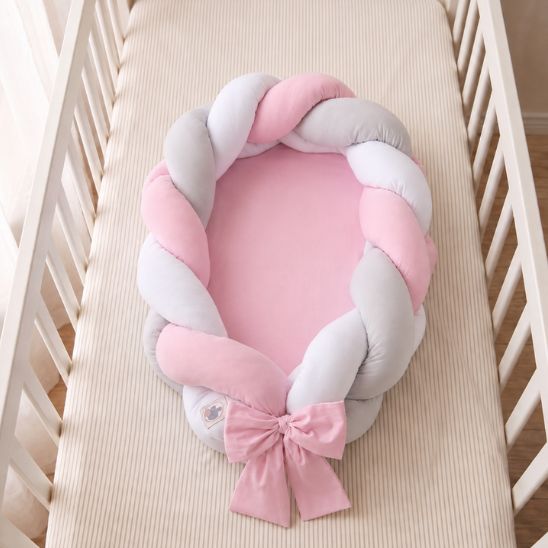 Réducteur de lit tressé rose avec matelas rose, vu de dessus dans un lit à barreaux