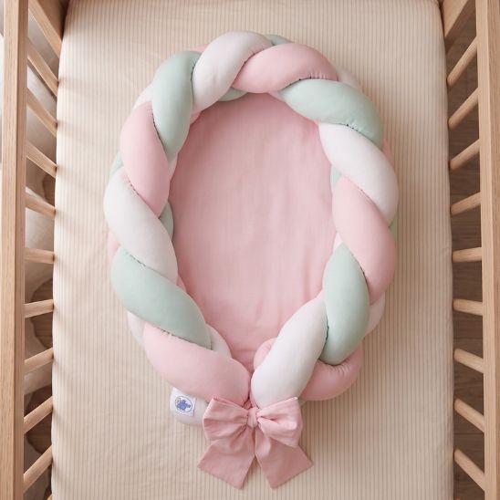 Réducteur de lit tressé rose, menthe et blanc vu de dessus dans un lit à barreaux