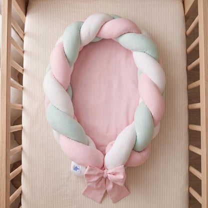 Réducteur de lit tressé rose, menthe et blanc vu de dessus dans un lit à barreaux